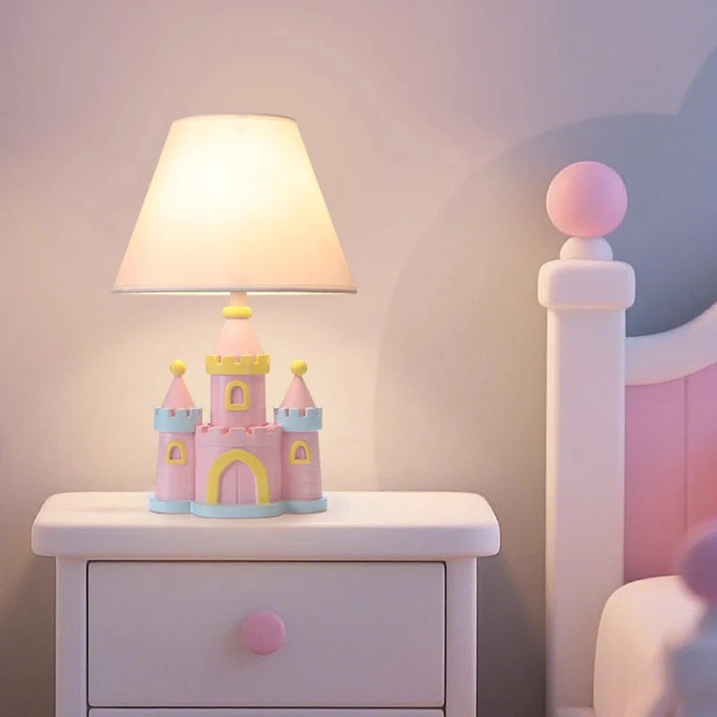 A pink castle table lamp with a conical off-white fabric shade rests on a white bedside table beside a pink bed frame.