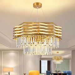 A gold tiered crystal chandelier illuminated in a dining room setting with blue chairs and a dark table.