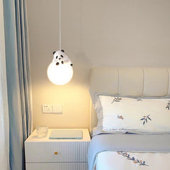 A white panda figurine hangs on a globe pendant light fixture above a bedside table in a softly lit bedroom.