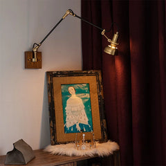 Wall sconce with brass finish and black swing arm positioned over a framed picture on a shelf.