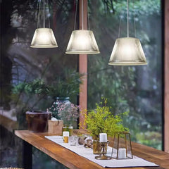 Three clear pleated glass drum pendant lights hanging over a wooden table with plants.