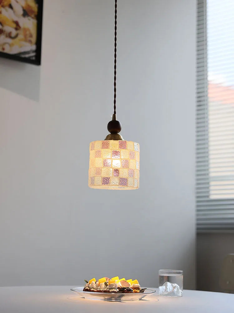 Small pendant light with a checkered glass shade hanging above a table with food.