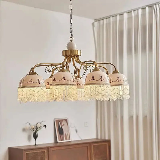 Gold floral ceramic pendant light with white tassels hanging from a chain, illuminated.