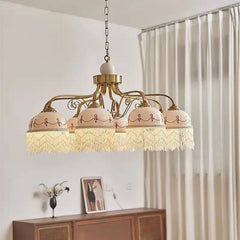 Gold floral ceramic pendant light with white tassels hanging from a chain, illuminated.