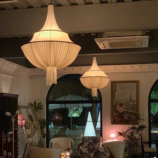 Two white fabric pleated pendant lights with black trim hanging in a room with arched windows and artwork on the walls.