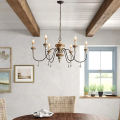 Distressed wood and iron chandelier illuminating a dining room with exposed beams and a table.