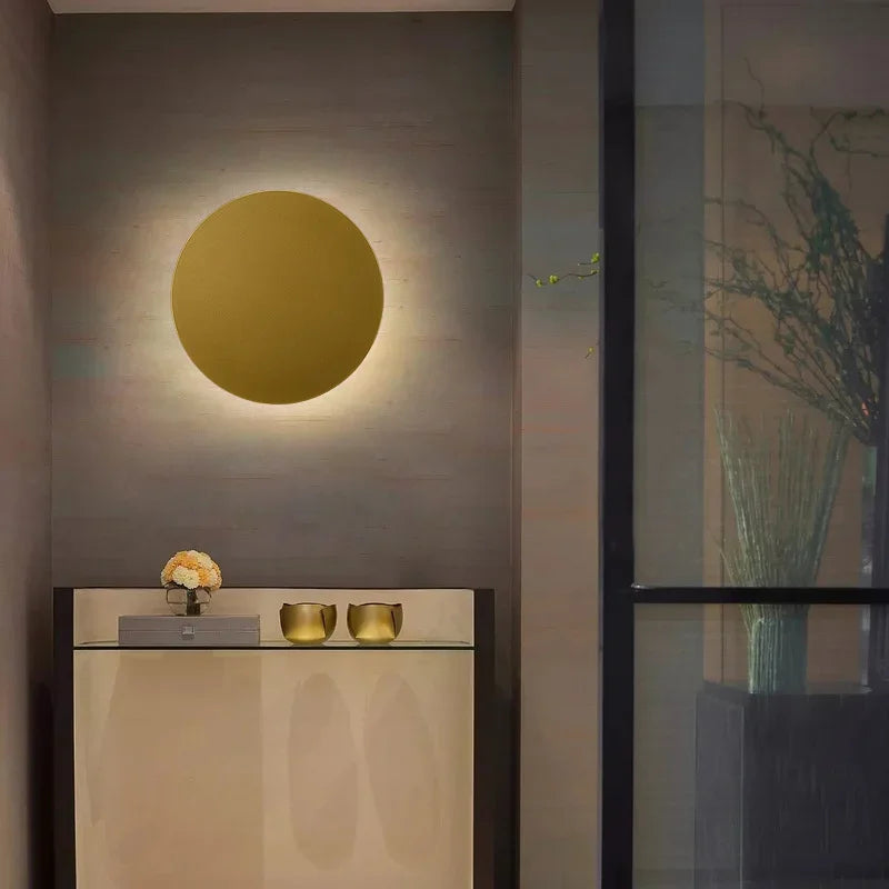 A gold circular wall sconce mounted above a console table with decorative items.