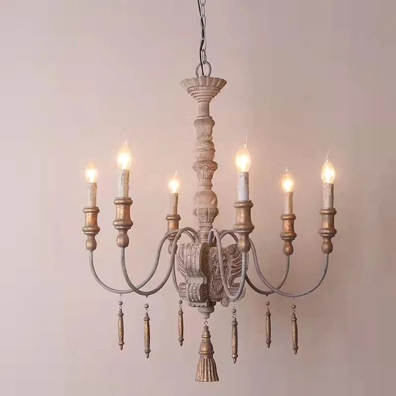 Close-up view of a distressed wood chandelier featuring carved details and candle-style light fixtures against a neutral background.