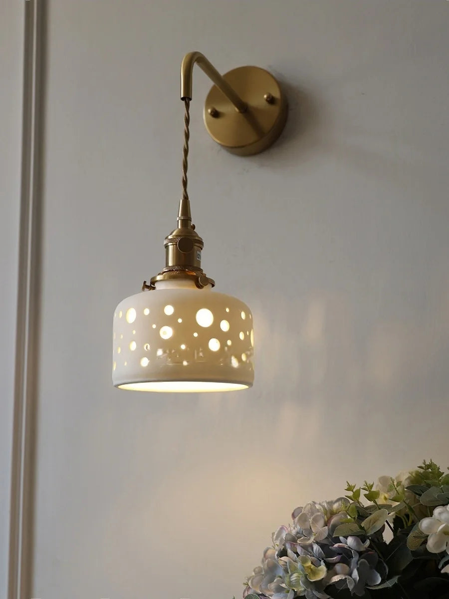 Wall-mounted lamp with decorative white shade and gold fixture on a light gray wall.