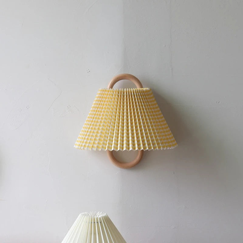 A yellow and white checkered fabric cone shade wall sconce with a natural wood hoop frame mounted on a textured white wall.