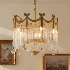 Close-up view of a gold chandelier with cascading crystal elements and glass rods, hanging in a room with framed artwork.