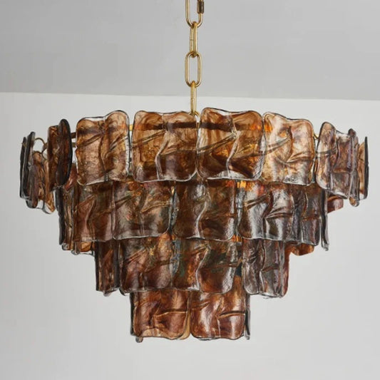 A multi-tiered chandelier with square, textured amber glass panels suspended from a gold chain and frame, against a white ceiling and wall.