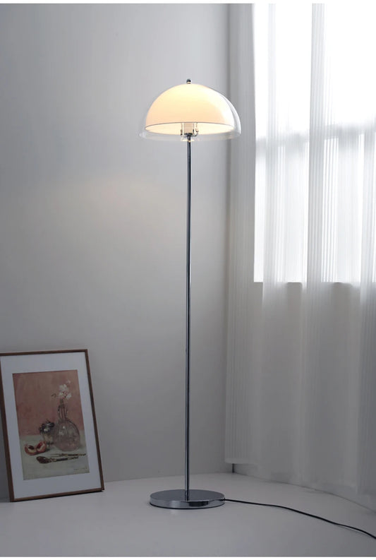 A tall, slender floor lamp with a clear dome shade and a metal base in a softly lit room.