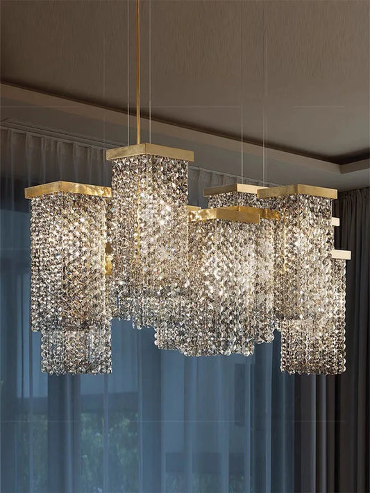 Gold crystal waterfall pendant light with cascading teardrop crystals hanging from a rectangular gold frame, illuminating a room with soft light.