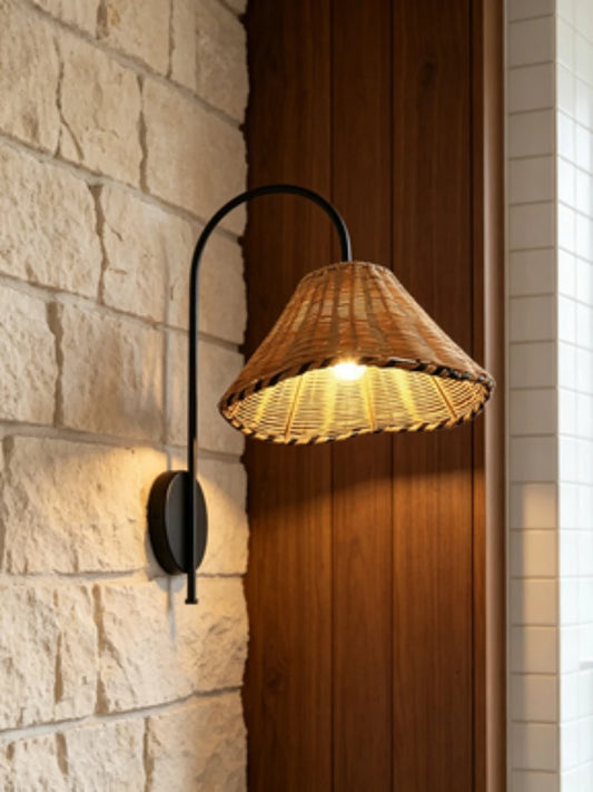 Black metal arm wall sconce with a woven rattan cone shade mounted on a stone wall next to a wooden panel.