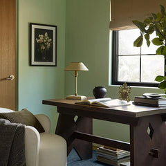 A black metal table lamp with a cone shade and polished chrome details, shown in a dimly lit room setting.