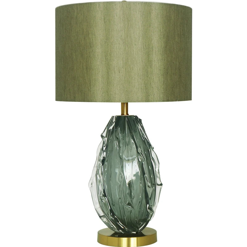 Decorative table lamp with a textured green glass base and beige lampshade on a white background