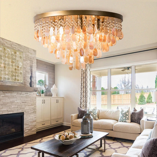 Gold shell and crystal cascading pendant light installed in a modern living room with a stone fireplace and sofas.