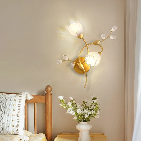 Close-up of a gold floral leaf wall sconce with a white glass shade and crystal accents.