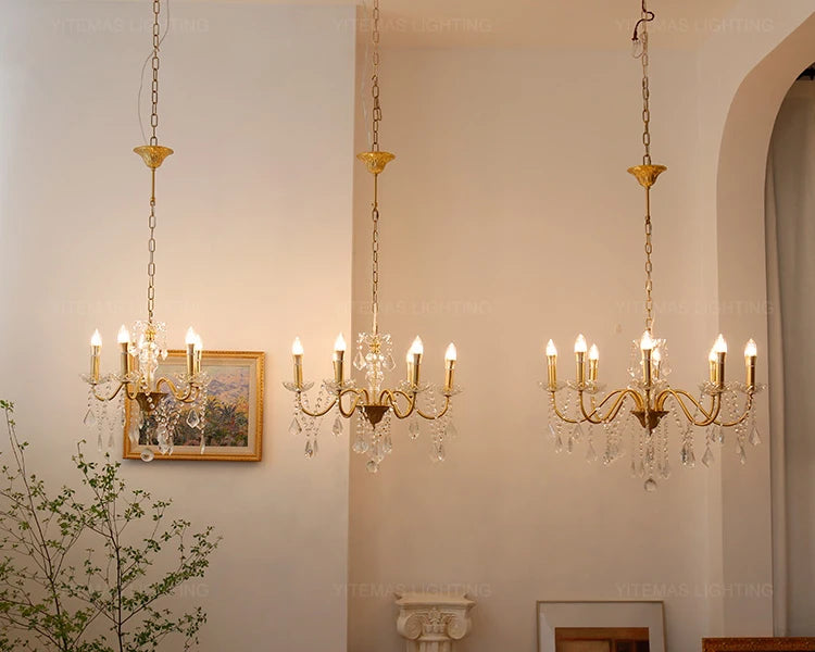 Three gold chandeliers hanging in a room with a neutral wall and decorative elements.