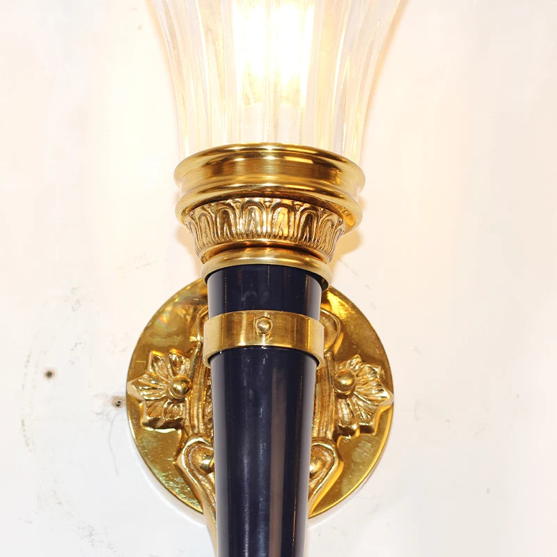 Close-up view of the mounting plate and lower body of a gold wall sconce, showing ornate details and a dark conical section.