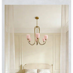 Brushed gold chandelier with pink tulip glass shades suspended over a bed.