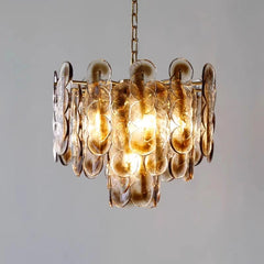 A pendant light with amber glass discs and a gold frame, shown against a neutral background.