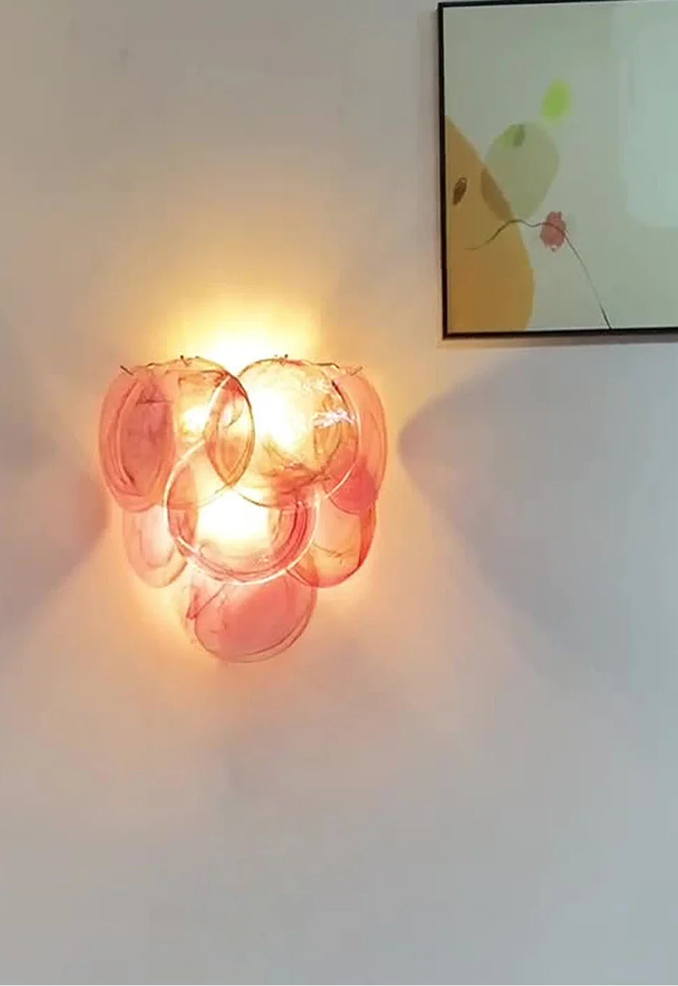 Wall-mounted lamp with pink glass shades on a white wall with a framed picture above.