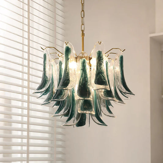 Close-up of a gold-tone tiered chandelier with cascading green and clear glass elements, illuminated by warm light.
