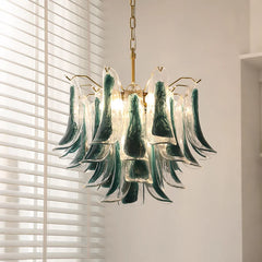 Close-up of a gold-tone tiered chandelier with cascading green and clear glass elements, illuminated by warm light.
