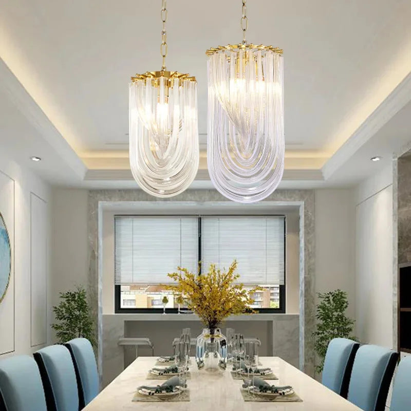 Two pendant lights, one gold and one chrome, with U-shaped clear glass tubes, hanging over a dining table.