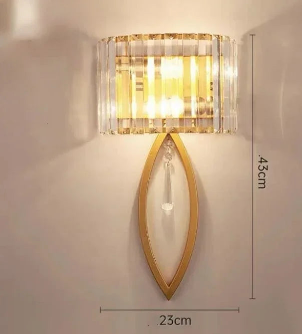 Wall-mounted light fixture with gold frame and clear glass shade on a white wall, showing dimensions.