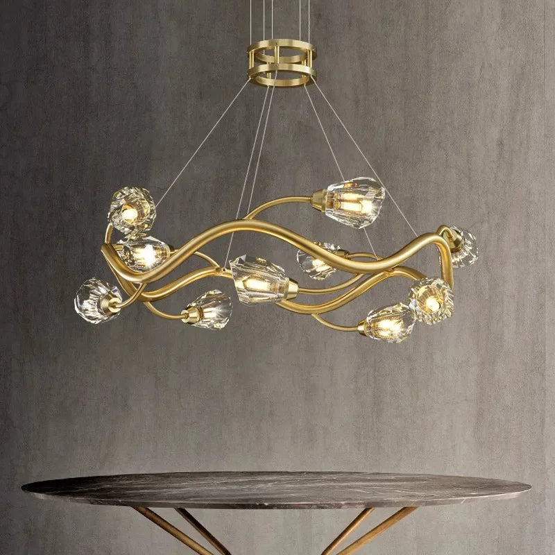 A single-tier gold wavy crystal chandelier with crystal accents, suspended above a marble-topped table.