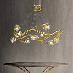 A single-tier gold wavy crystal chandelier with crystal accents, suspended above a marble-topped table.
