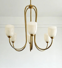 A gold-toned chandelier with five white glass shades against a white background.
