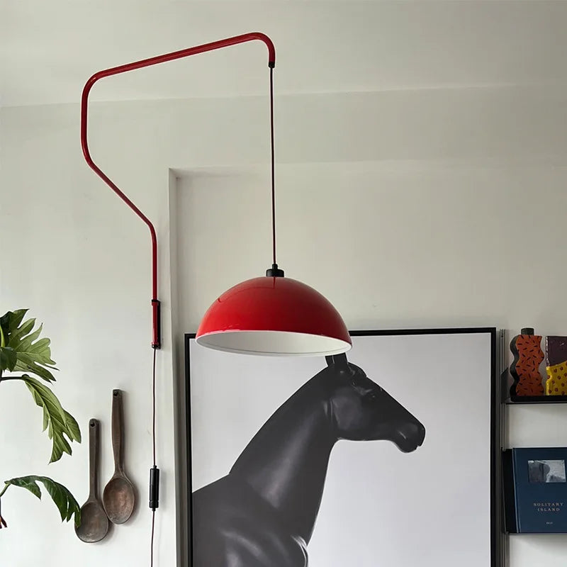 Close-up of a red folding retractable wall lamp with a dome shade, featuring a black cord and switch, with a large black horse art print in the background.