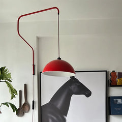 Close-up of a red folding retractable wall lamp with a dome shade, featuring a black cord and switch, with a large black horse art print in the background.