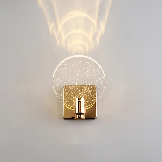 Close-up of a gold and clear bubble crystal wall sconce mounted on a white wall, showing its round shade and square base.
