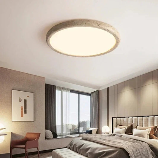 A circular flush mount ceiling light with a textured, stone-like beige frame and a smooth white diffuser, installed in a modern bedroom.