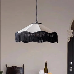 A black tassel fabric pendant light with a scalloped shade hanging above a dining area, with a bottle of wine visible in the foreground.