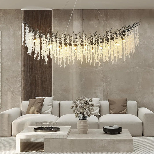A wide, curved chandelier with crystal teardrops hanging, suspended over a large sectional sofa in a living room.