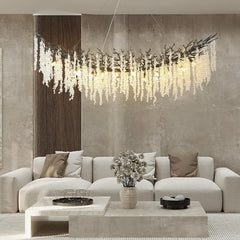 A wide, curved chandelier with crystal teardrops hanging, suspended over a large sectional sofa in a living room.