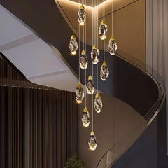 Close-up view of a cascading gold chandelier, showing the intricate detail of the faceted crystal drops and their warm LED illumination against a blurred modern interior.