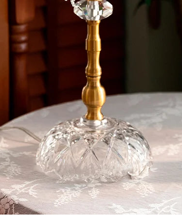 Decorative glass and gold candle holder on a lace tablecloth with flowers in the foreground.