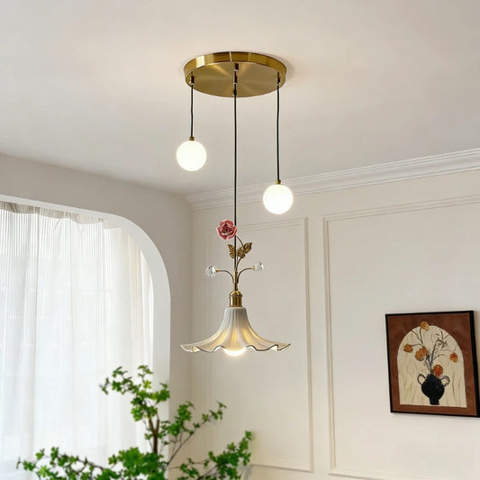 Gold floral rose bud ceramic pendant light with two white globe lights hanging from a brass circular canopy