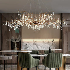Dining room with a large, cascading brass chandelier with clear teardrop crystals, a marble-topped table, and green upholstered chairs.