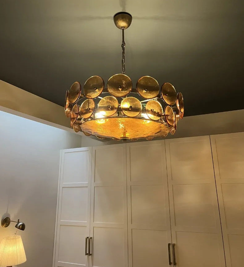 Gold chandelier hanging in a room with white cabinets and a lamp.