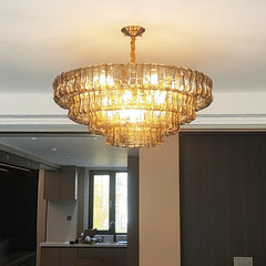 A multi-tiered gold chandelier with amber glass accents shown in an interior setting, with a glimpse of a kitchen area.