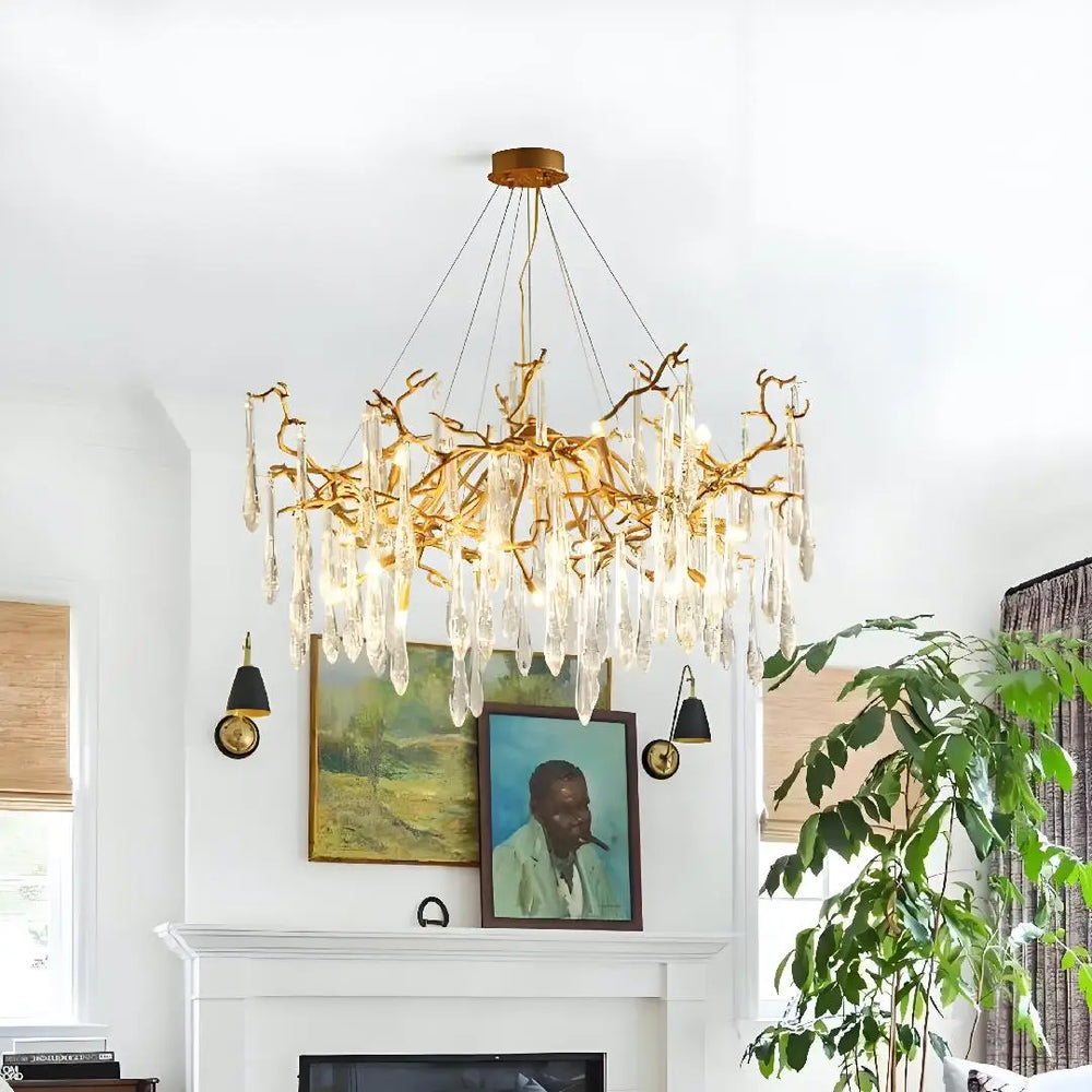 Gold chandelier hanging above a fireplace with framed pictures and a plant in the background.