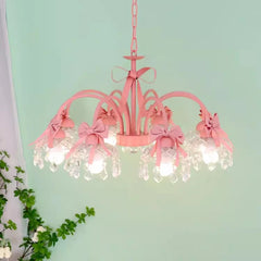 Side view of a pink chandelier with pink bows and crystal accents, suspended against a light green wall.